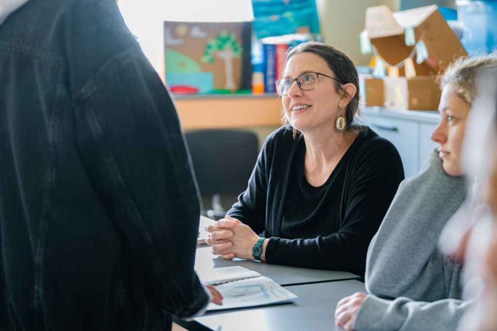 A college professor wearing glasses smiles up at a student