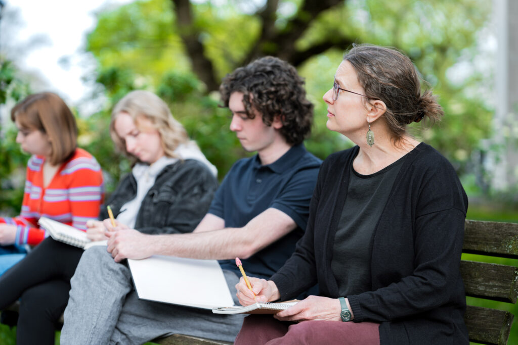 A college professor and students sit outside and write