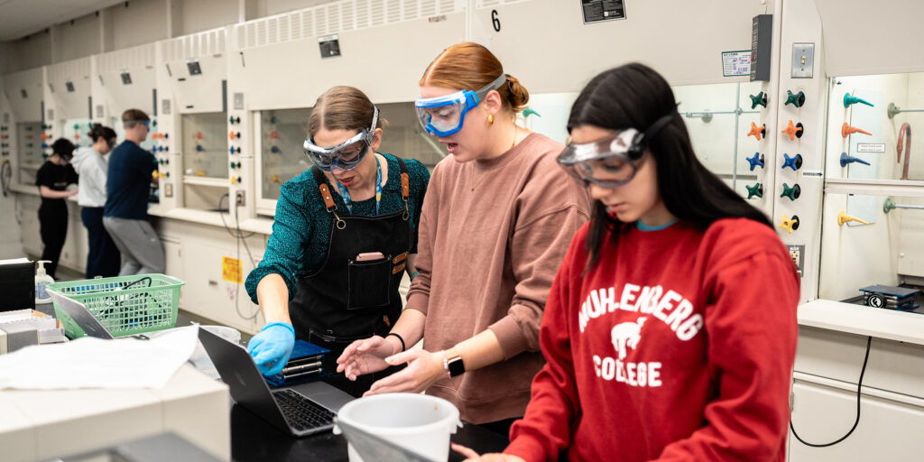 A college professor and students in goggles work in a chemistry lab