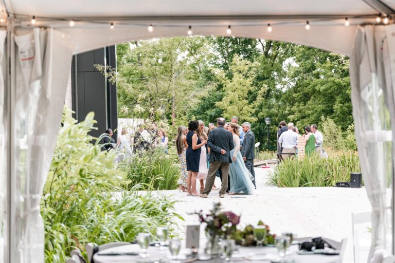Wedding attendees gather on a patio next to a white tent
