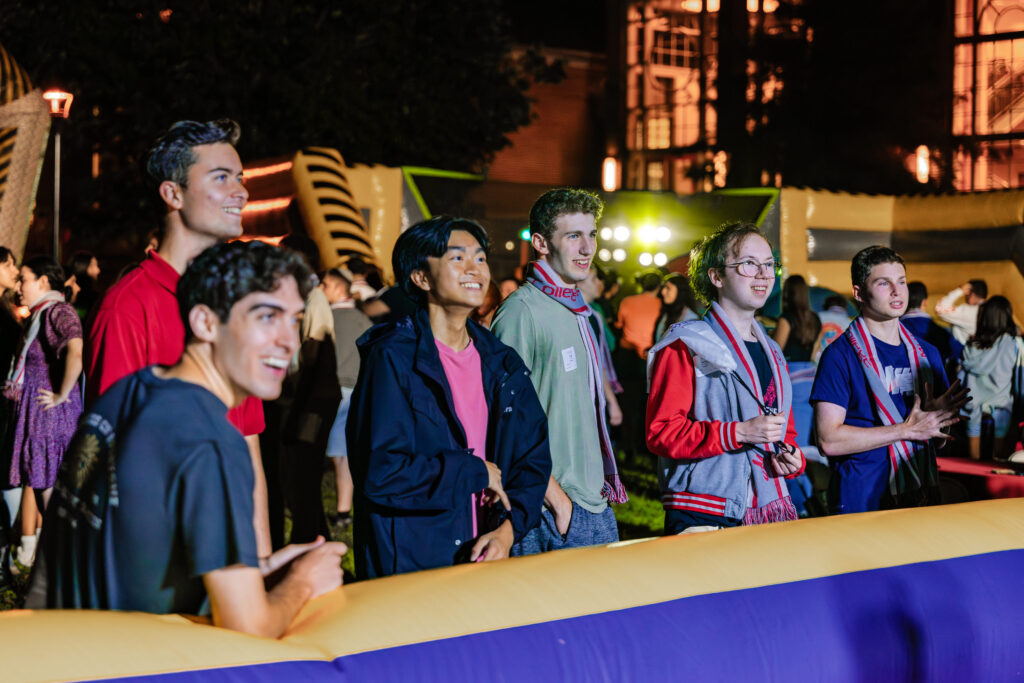 A bunch of college students watch other students take part in games outside at night