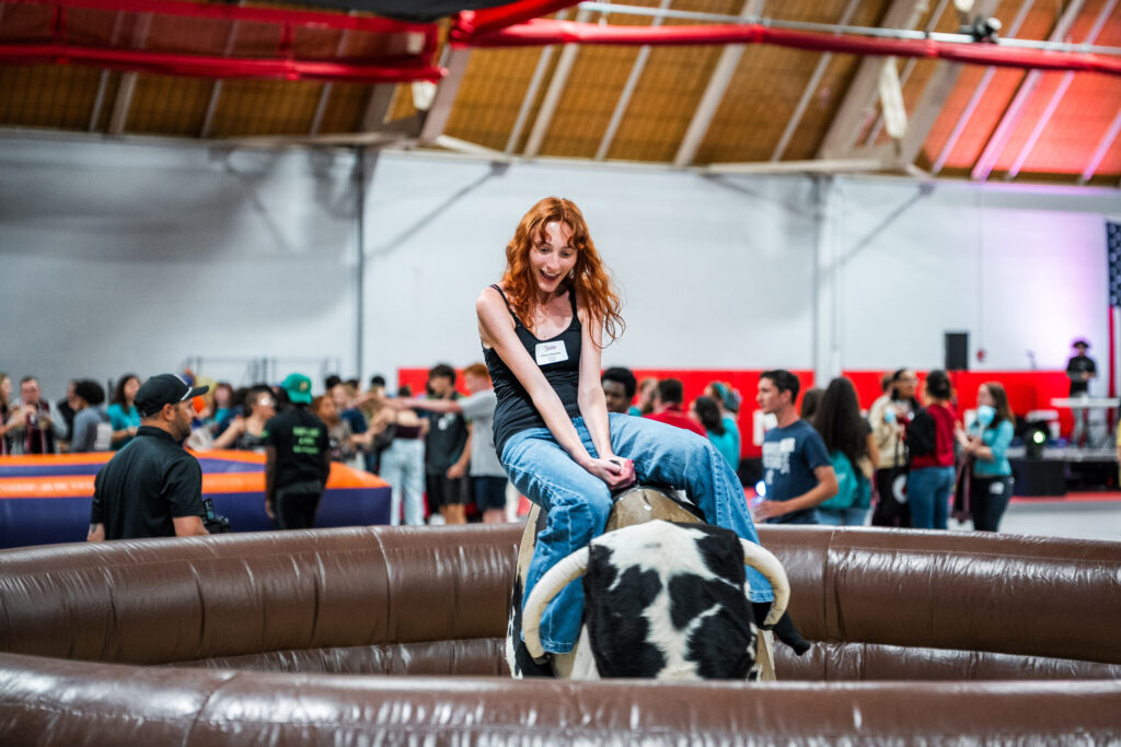 A college student rides a mechanical bull inside a gymnasium
