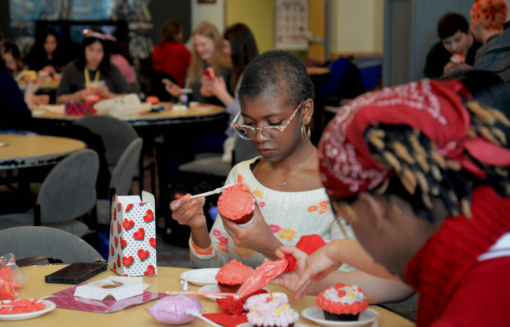 A college student wearing glasses frosts a cupcake