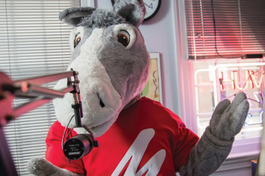 A college mule mascot speaks into a microphone in a radio studio