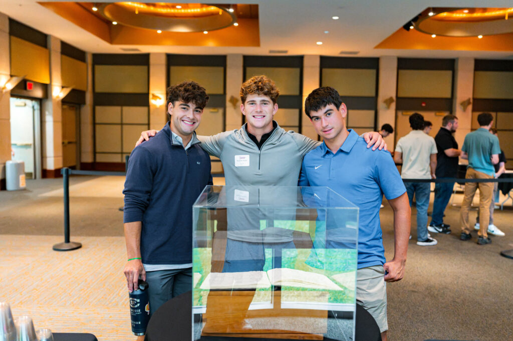 Three Muhlenberg College students stand in front of a glass display case with a book in it