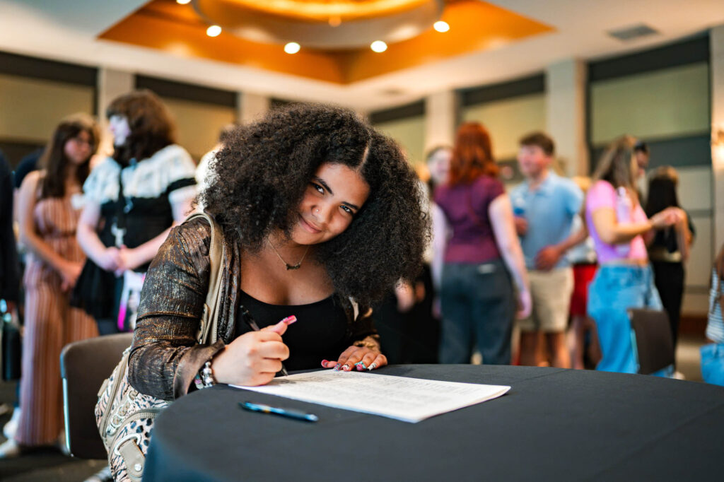 A Muhlenberg College student with long curly hair signs the matriculation ledger