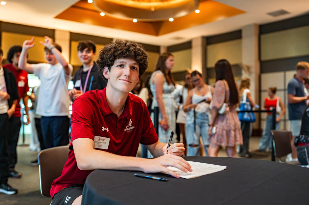 A Muhlenberg College student in a red shirt signs the matriculation ledger