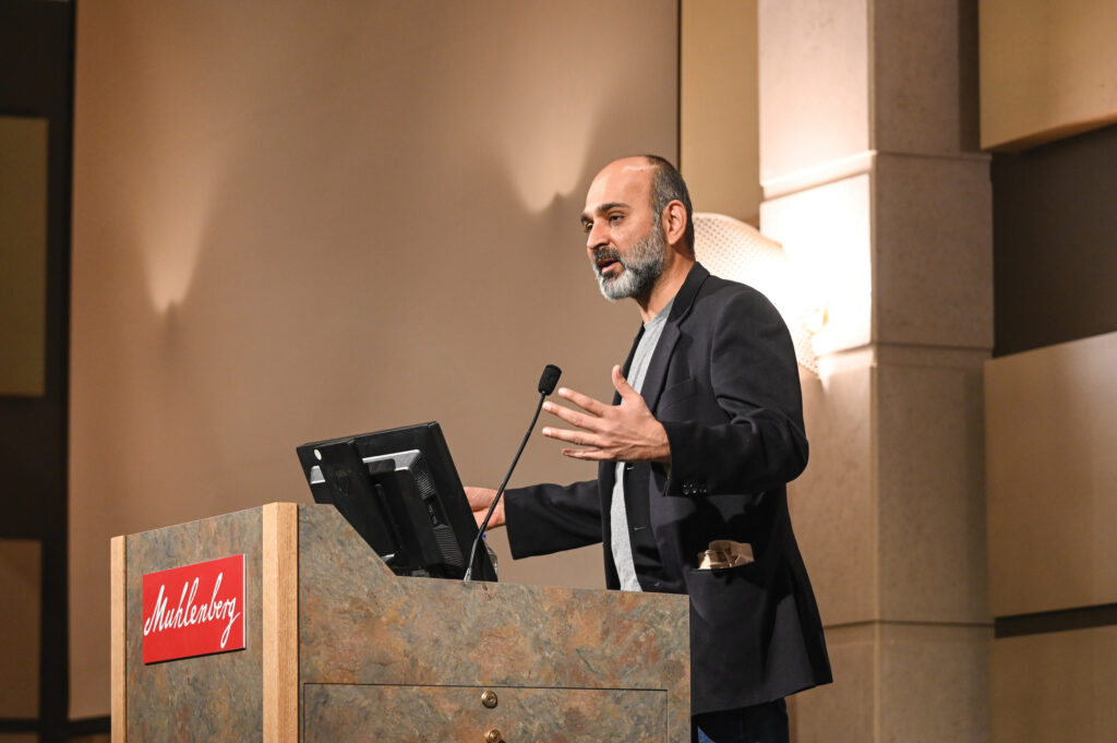 An author speaks at a podium that says Muhlenberg on the front