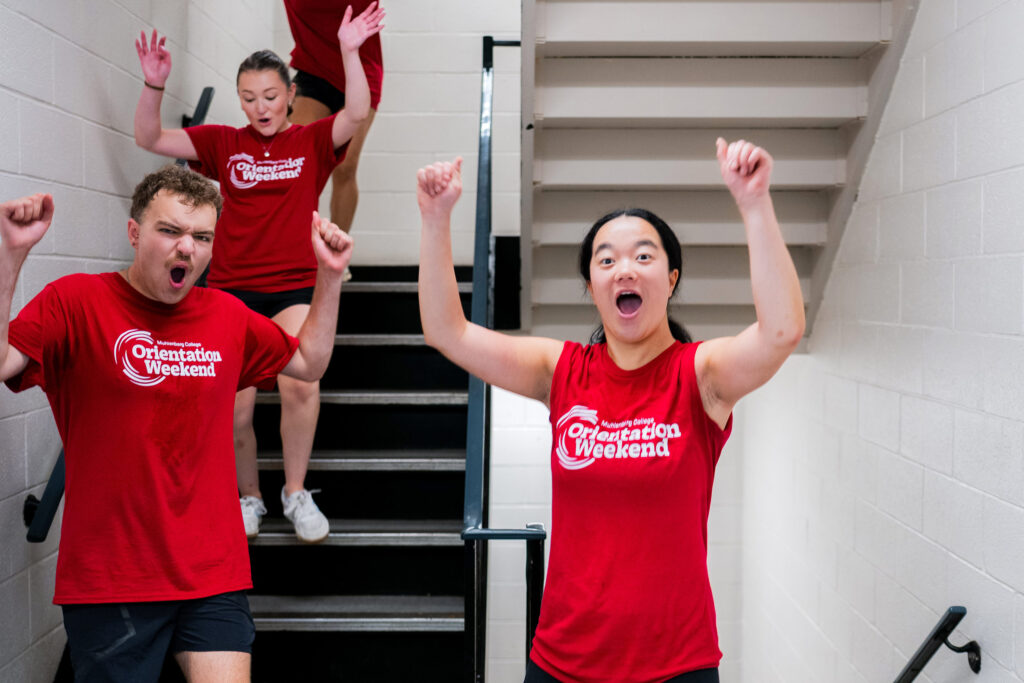 Muhlenberg College students in a stairwell in red T-shirts cheer during move-in