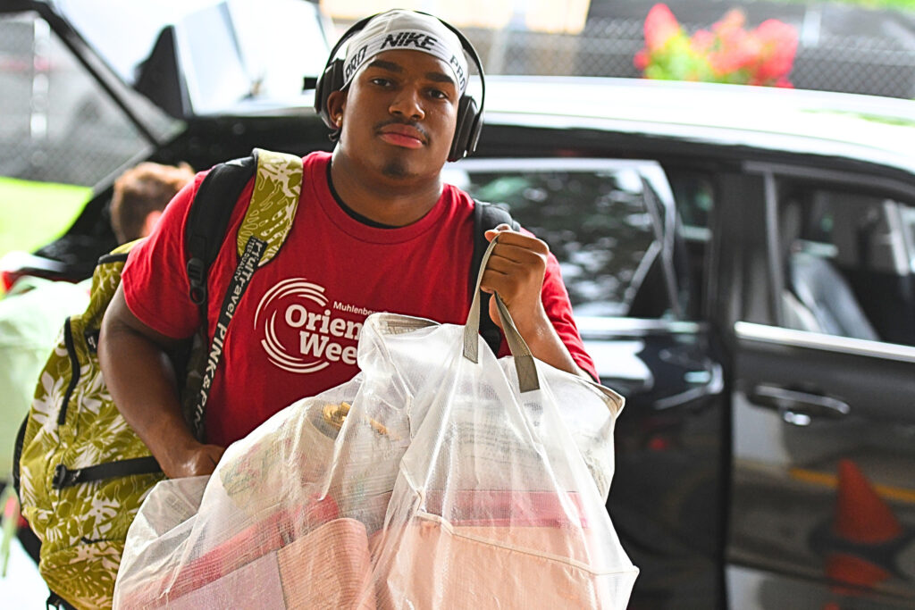 A Muhlenberg College student wearing headphones helps carry bags during move-in