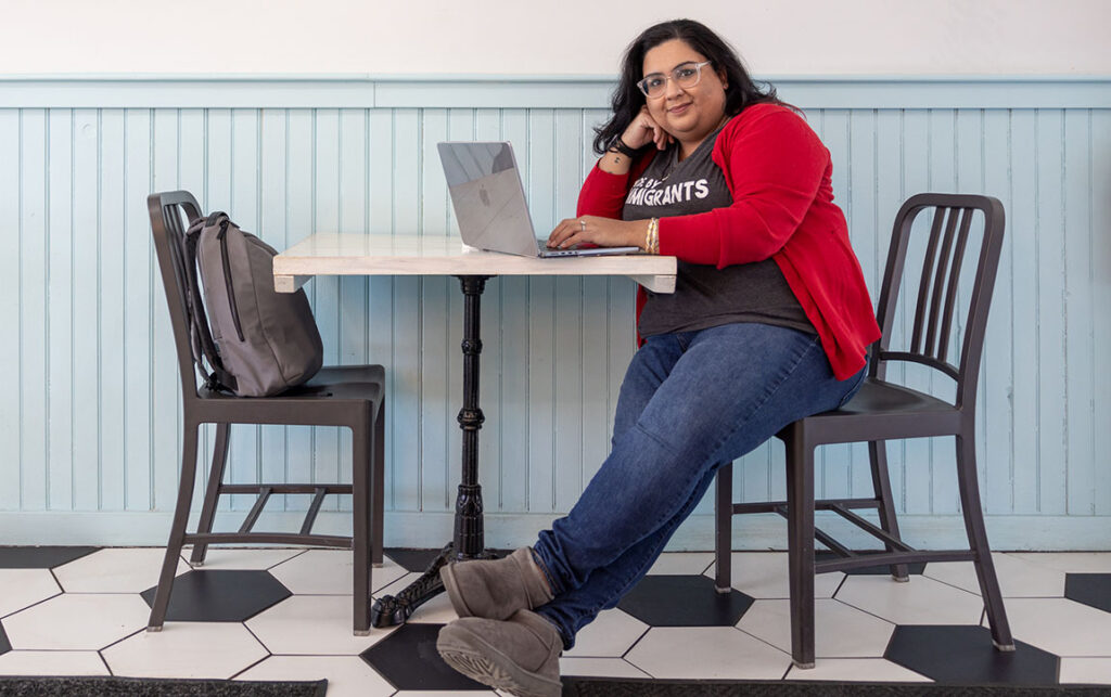 Nisha Sharma sits at a table with her laptop