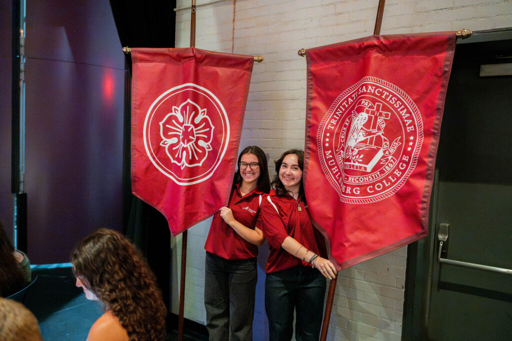 Two Muhlenberg College students hold up red banners with the college seal and the Luther rose