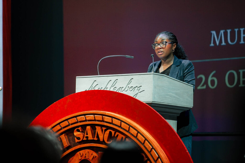 A Muhlenberg College student in glasses speaks at a podium