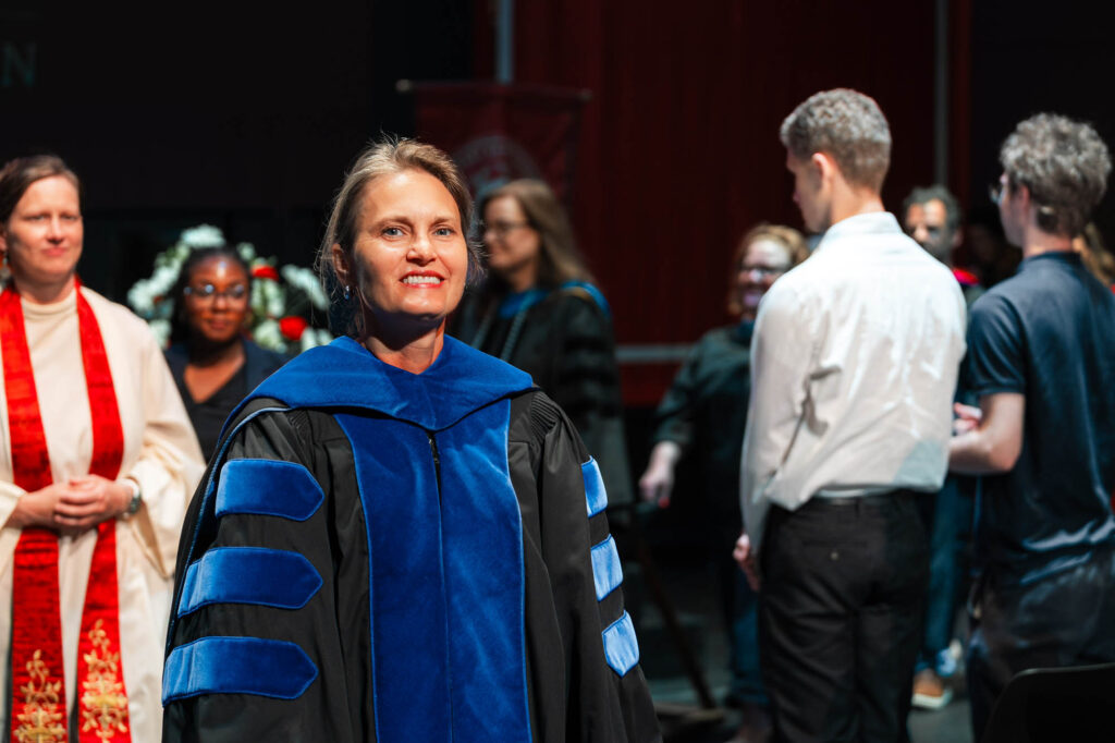 A Muhlenberg College administrator in academic regalia smiles at the camera