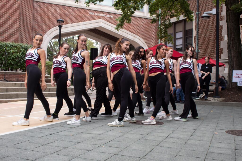 A group of college students on a dance team performs in matching outfits that say BERG on the front