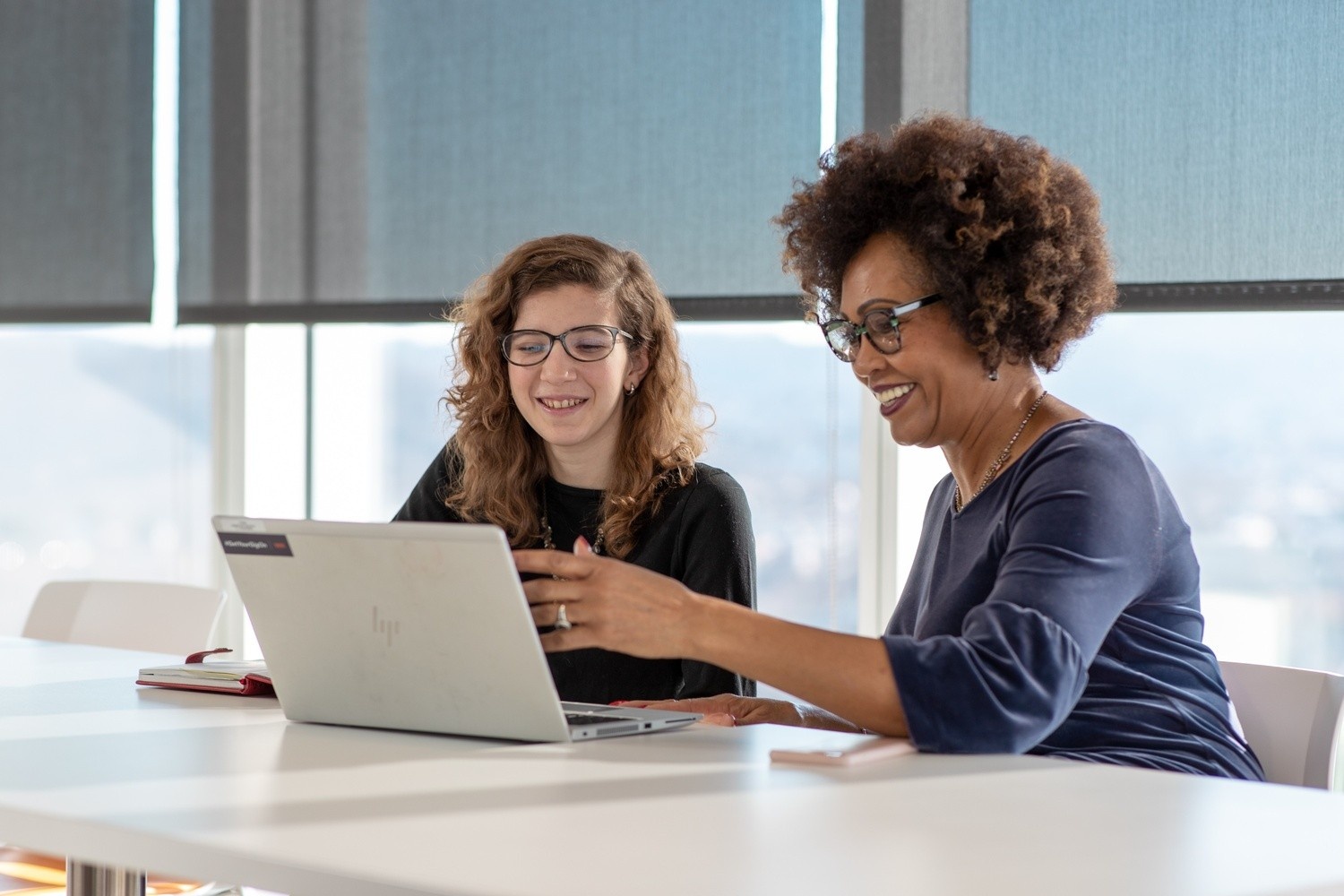 A student and a professional sit in an office working on laptop. 