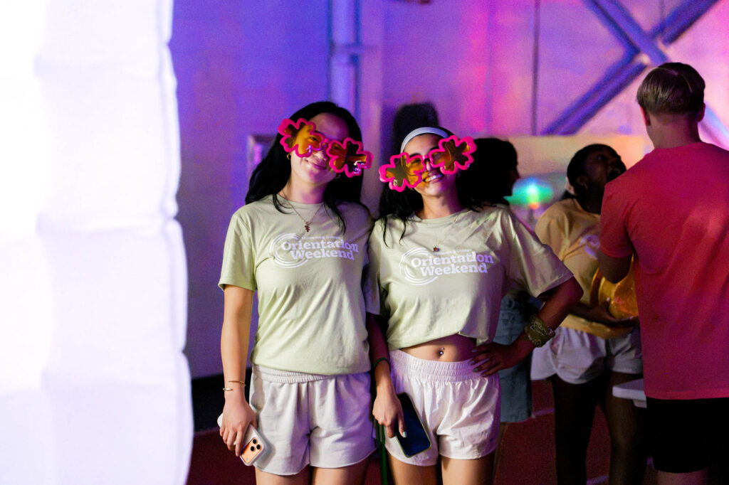 Two Muhlenberg College students in tan orientation shirts wear oversized pink sunglasses