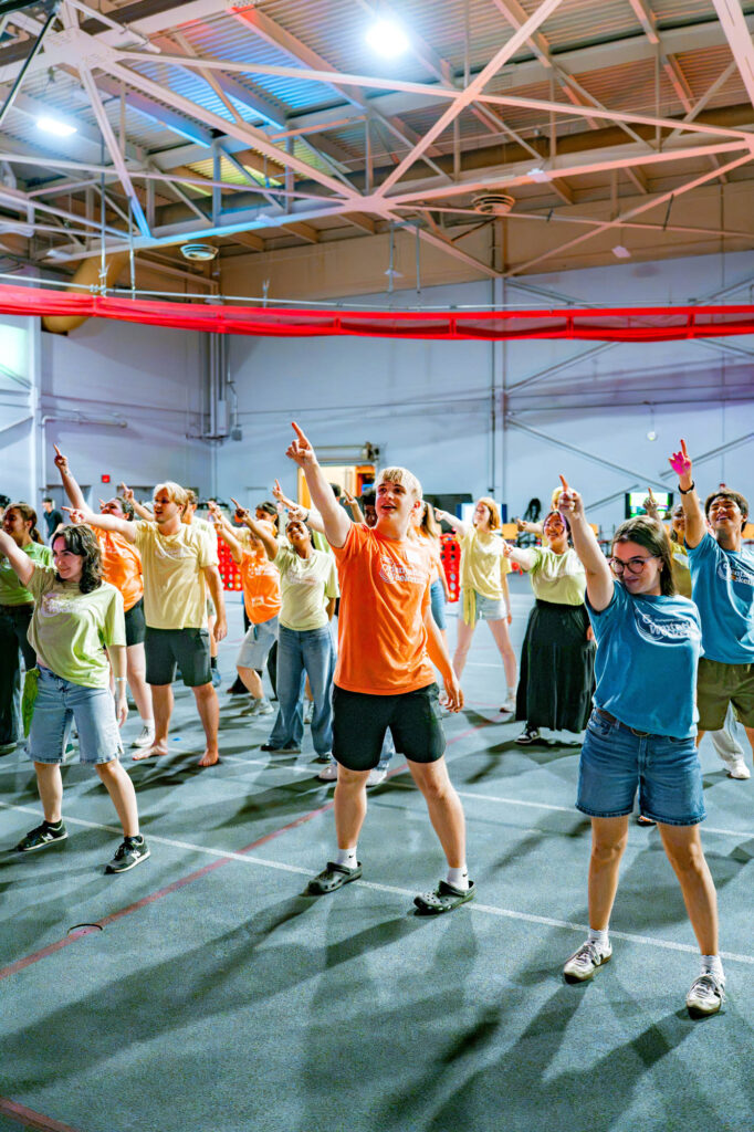 Muhlenberg College orientation leaders point while dancing during a welcome party in the field house