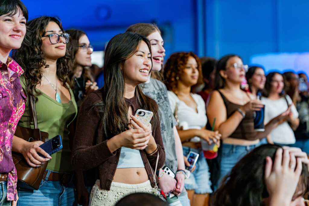 A group of new Muhlenberg College students smiles as they watch other students dance off-camera