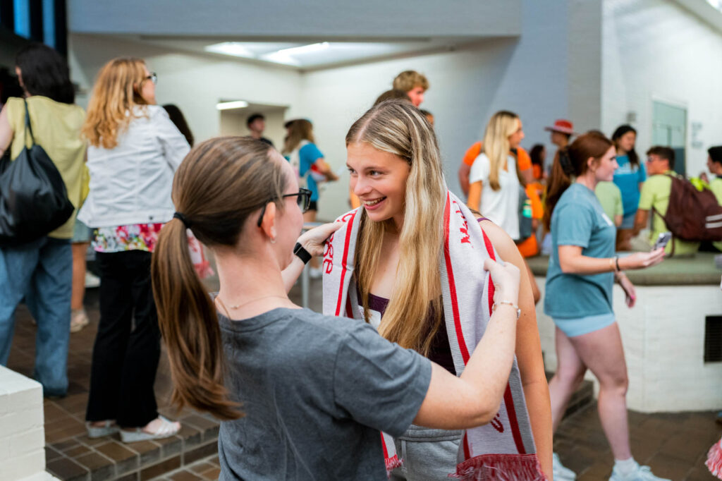 A Muhlenberg College alum drapes a scarf over a current student with long blonde hair