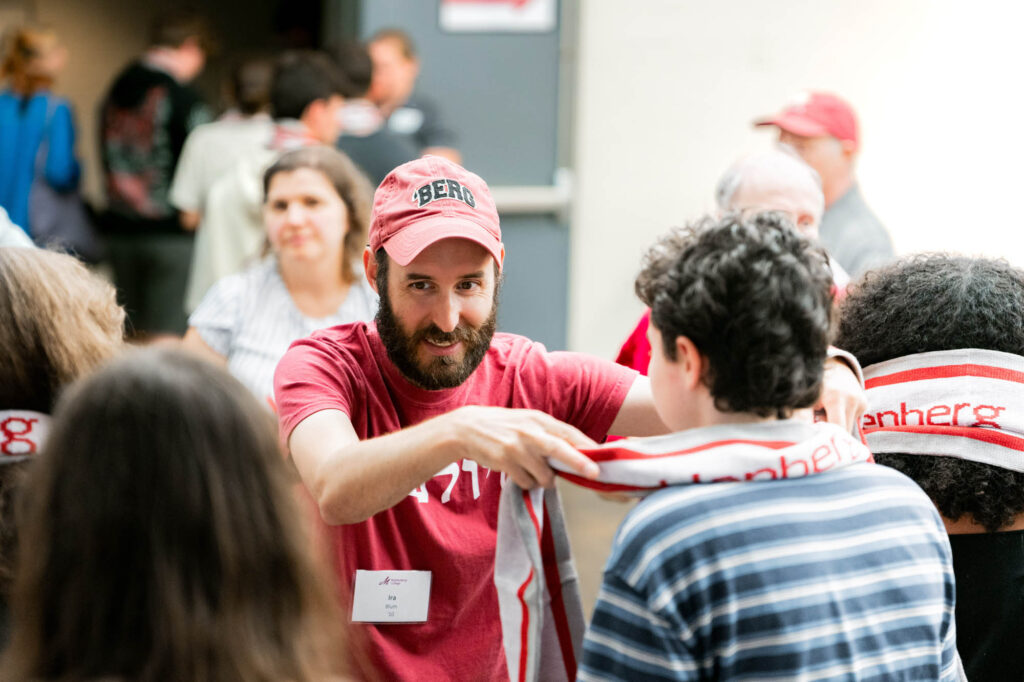 A Muhlenberg College alum in a baseball cap drapes a scarf over a current student with short dark hair