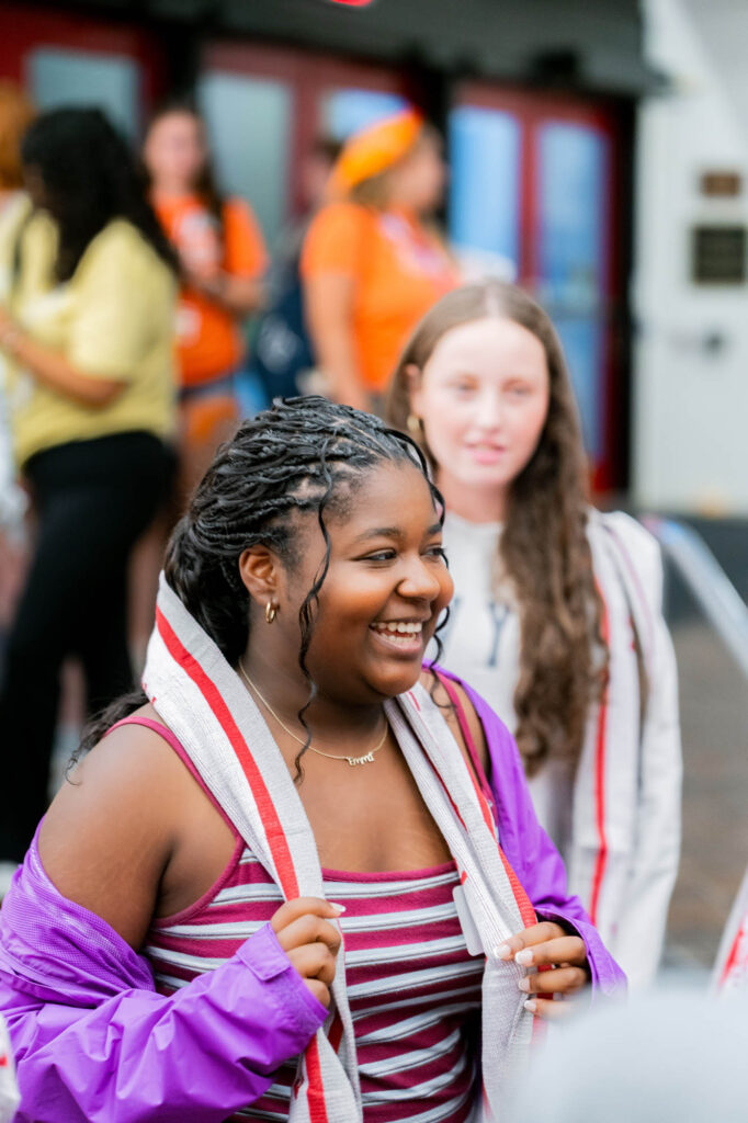 A Muhlenberg College student smiles while wearing a new red, white, and gray scarf