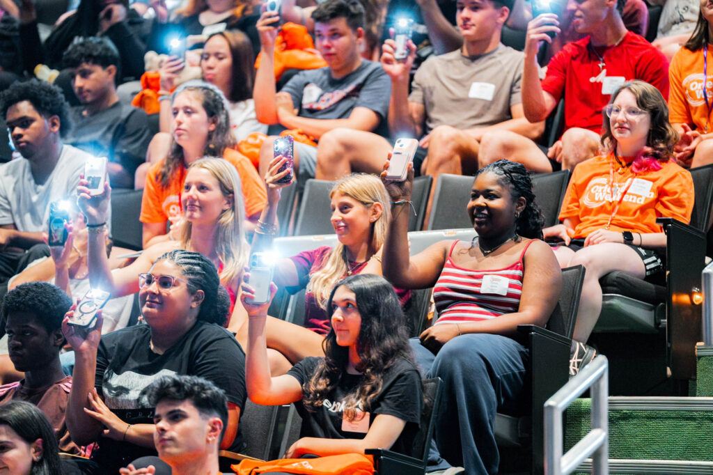 New Muhlenberg College students in an auditorium hold up their phones with their flashlights on