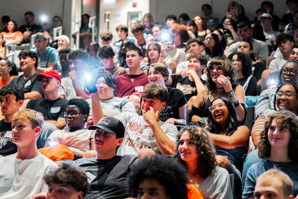 New Muhlenberg College students in an auditorium hold up their phones with their flashlights on