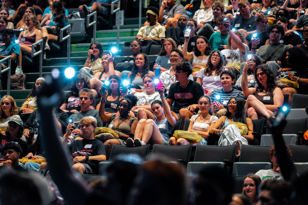 New Muhlenberg College students in an auditorium hold up their phones with their flashlights on