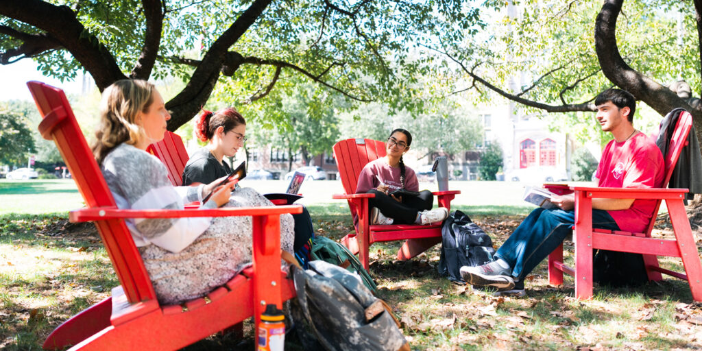College students sit in a circle in red Adirondack chairs