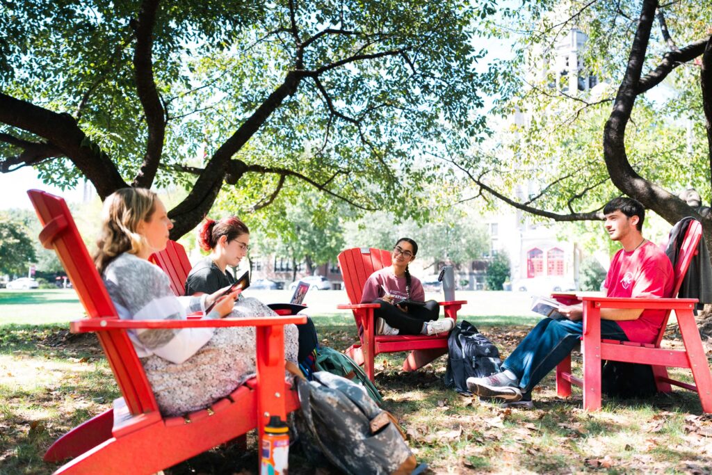 College students sit in a circle in red Adirondack chairs