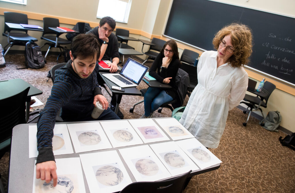 A Muhlenberg student studies artwork in a classroom, with a faculty member looking over his shoulder.