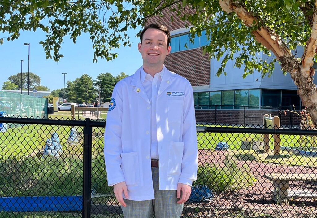 Muhlenberg student Tony Brach poses for a photo outdoors in a lab coat.