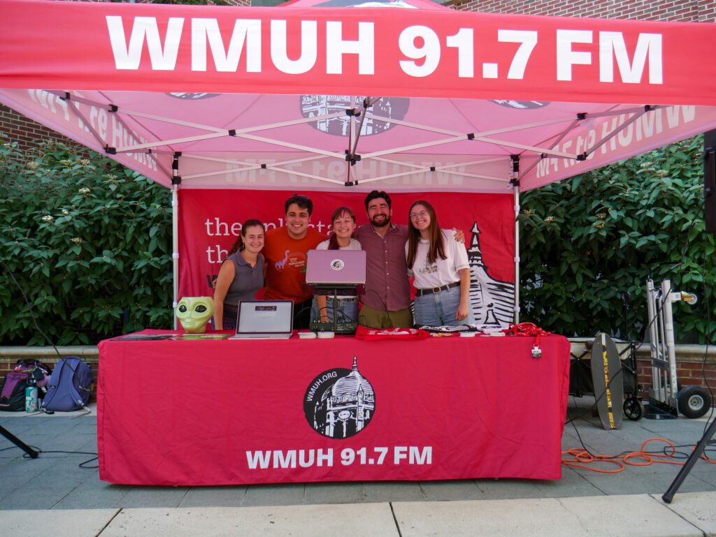 A group of college students stands under a red tent that says WMUH 91.7 FM