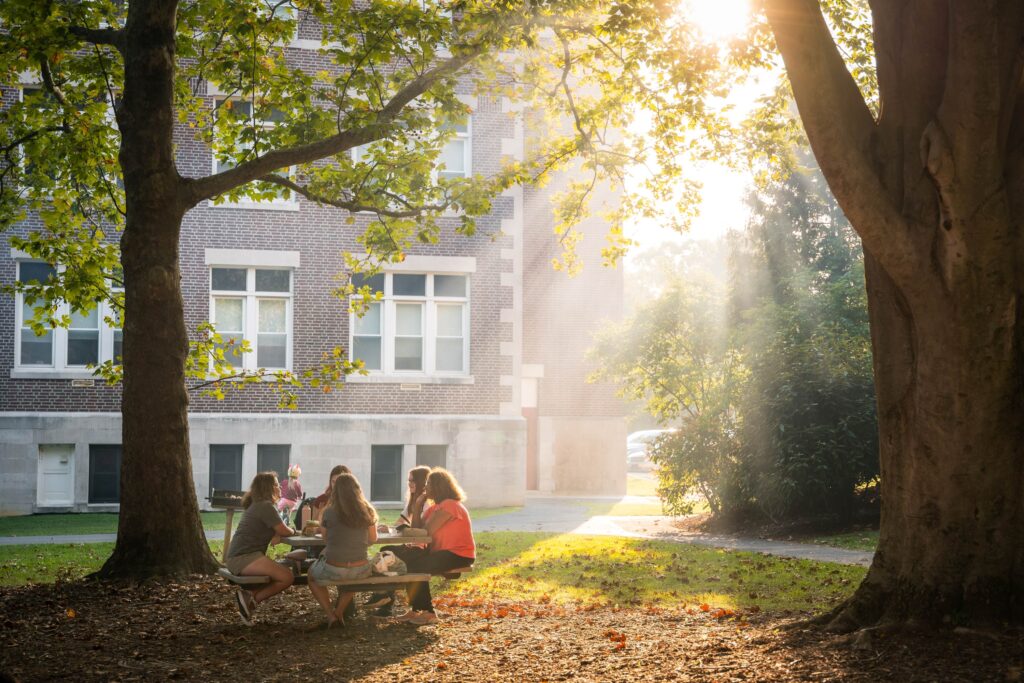 Sun filters through hazy air as college students sit at a table outside and converse
