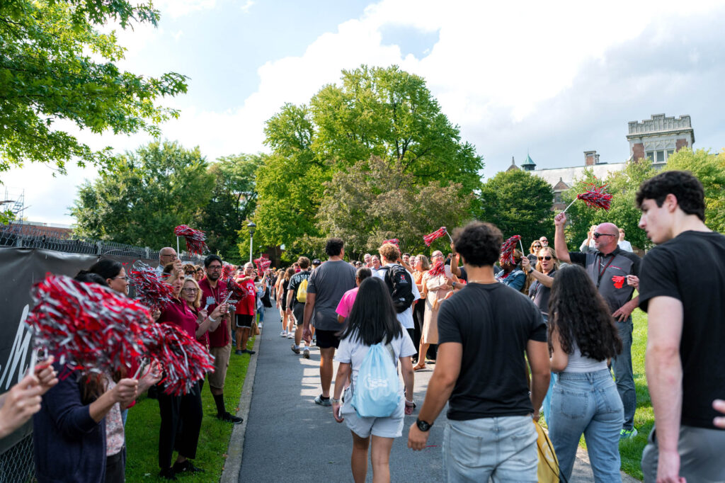 New Muhlenberg College students walk up a pathway between crowds lining the path cheering for them