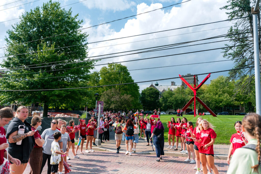 Muhlenberg College faculty and staff cheer on new students with the college green in the background