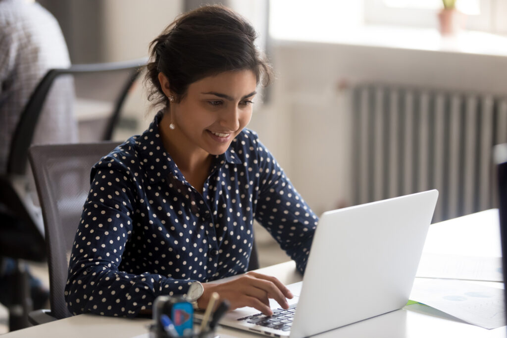A woman smiles while typing on a laptop.