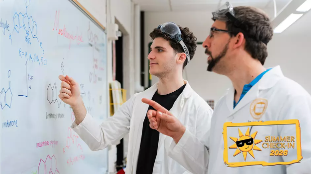 Zach Cohen looks at a chemistry white board alongside professor Ian MacKenzie