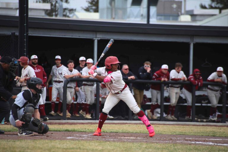 Mules Baseball teammates watch a batter from the dugout of Bicentennial Field on opening day.