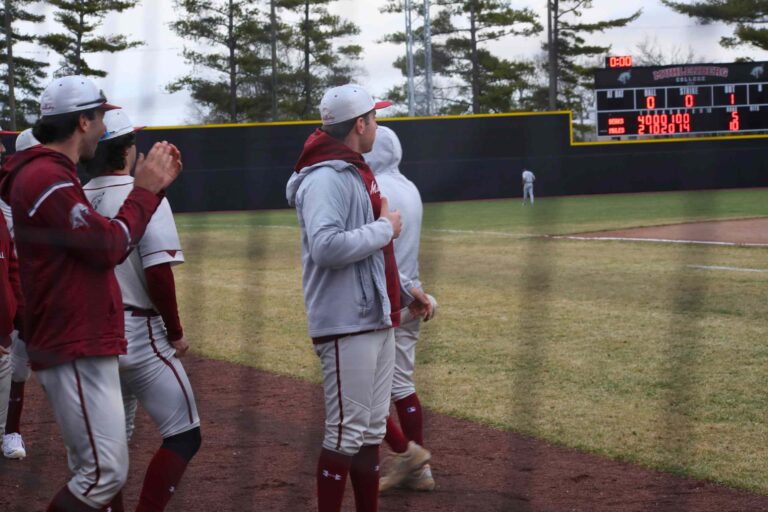 Mules Baseball players cheer on a runner, with the scoreboard showing Mules 10, Opponent 5 in the background.
