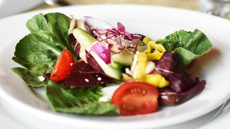 Dining Services A close up view of a mixed green salad with peppers and tomatoes
