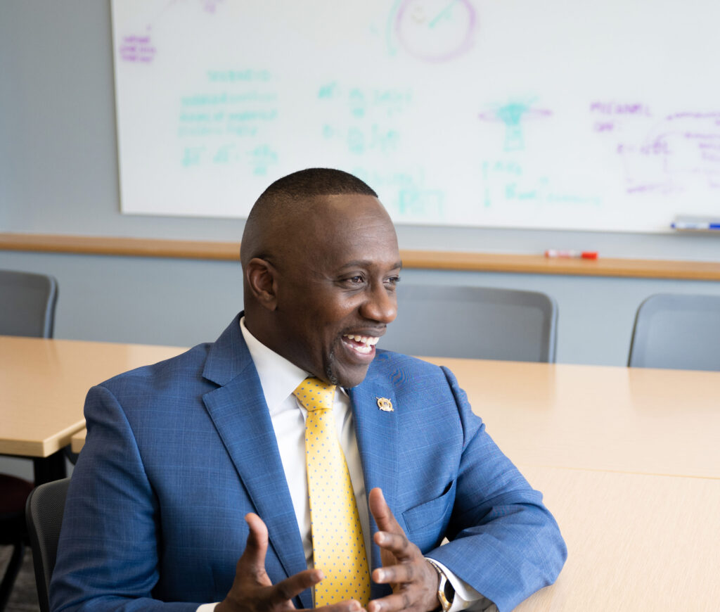 A man in a suit speaks at a table in a classroom.