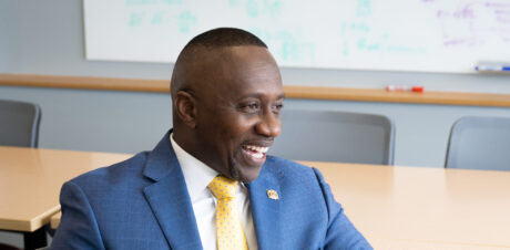 A man in a suit speaks at a table in a classroom.