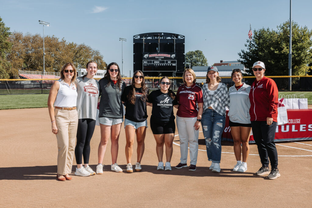 Several college athletes and a college president stand on a new softball field