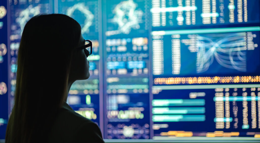 Silhouette of a woman looking at a large screen filled with data, charts, and maps.